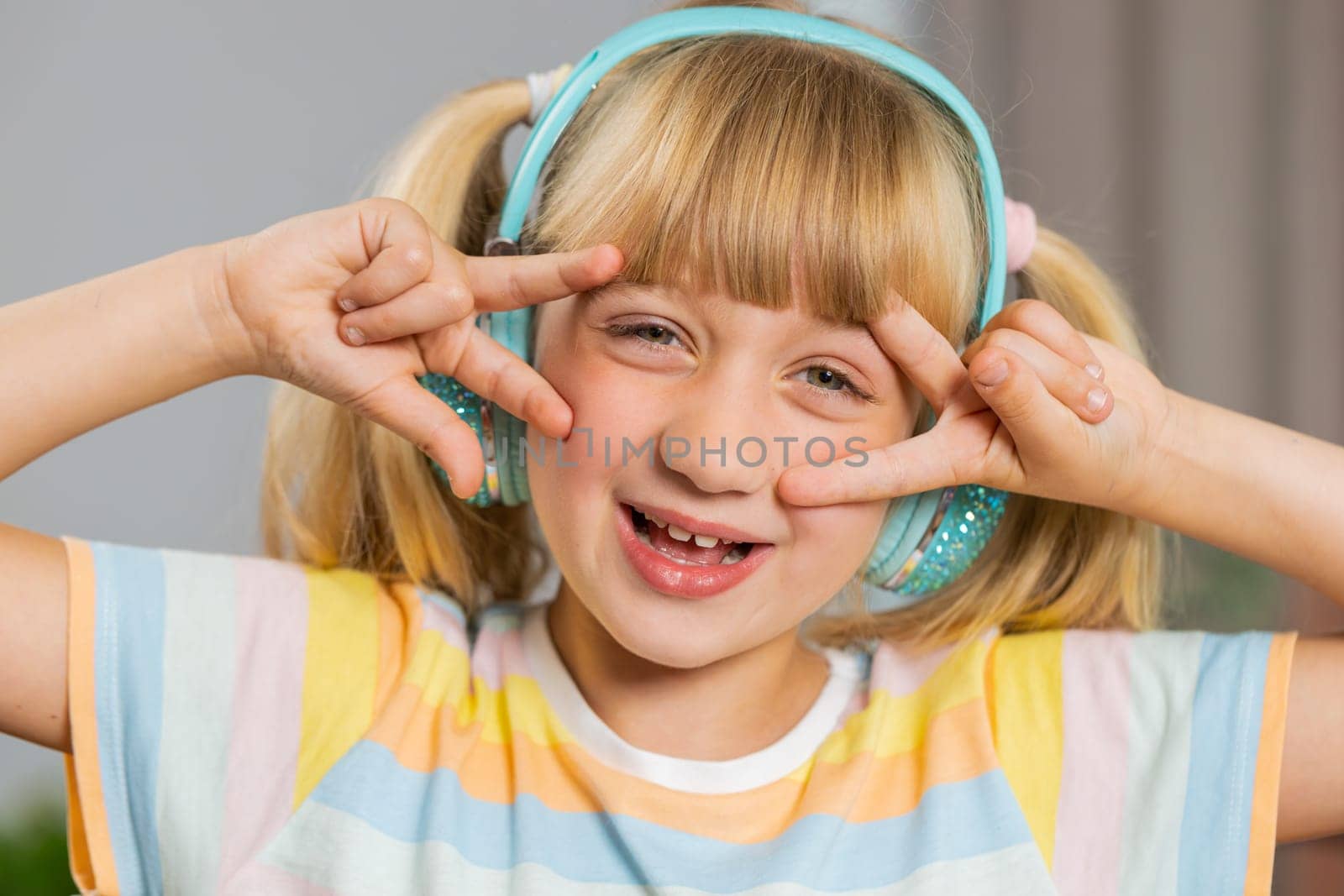 Portrait of happy overjoyed toddler girl kid in wireless headphones relaxing at home room choosing listening favorite energetic disco dancing music. Children weekends leisure activities. Lifestyles