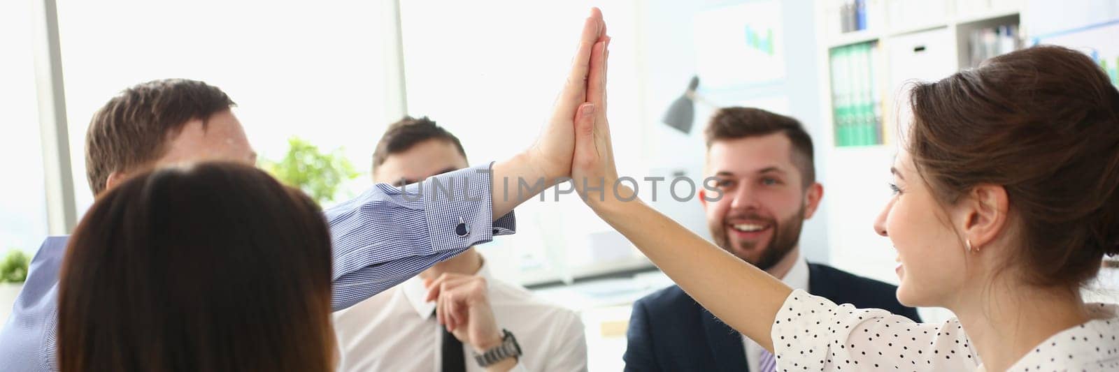 Enthusiastic teammates high-fives celebrate shared accomplishments and corporate success. Business people gathered at group meeting and team building concept