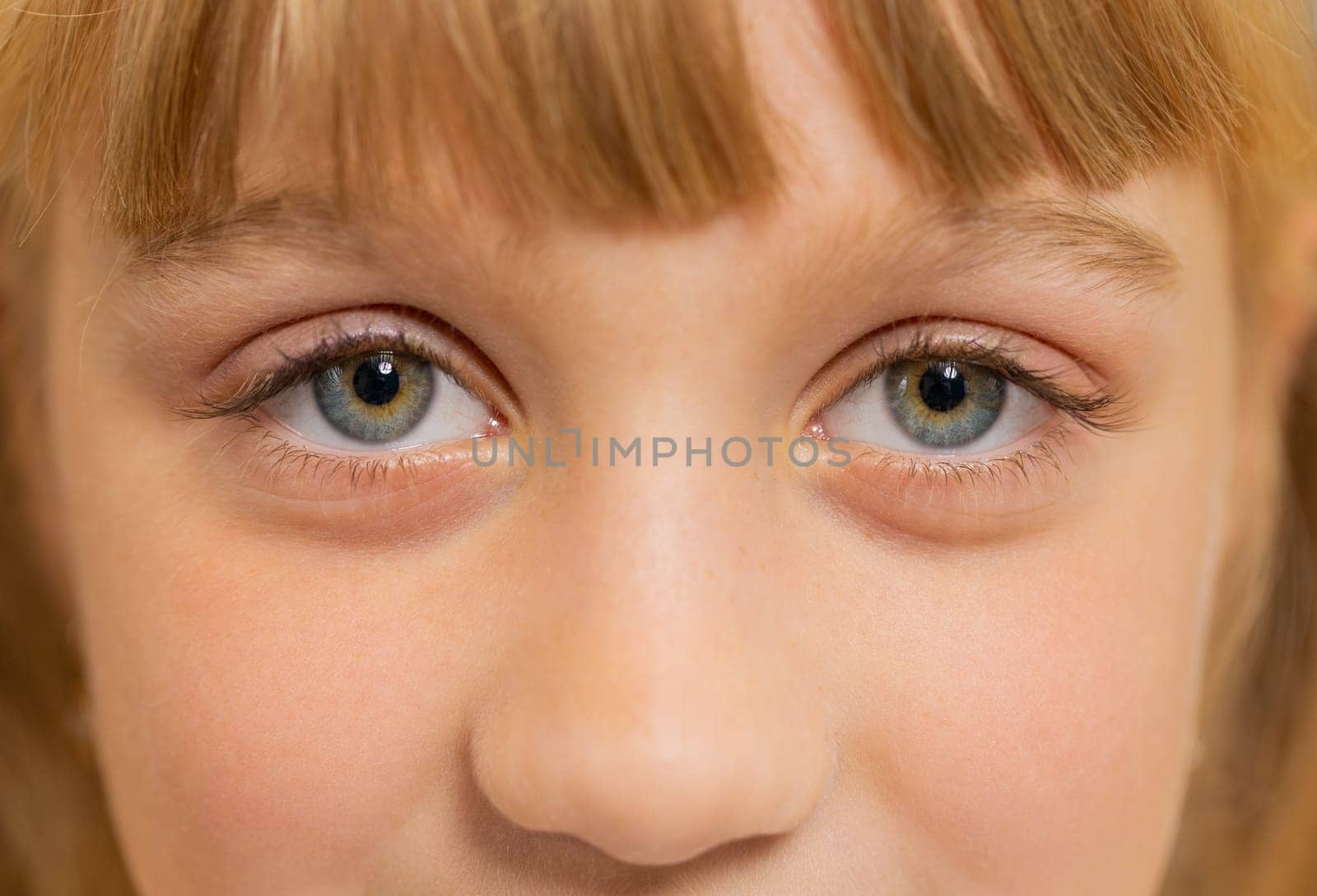 Extreme close-up macro portrait of smiling girl face. Teen beautiful kid's eyes looking at camera. Young positive toddler child opening wide her closed eyes. Gray eyes of blonde female children model
