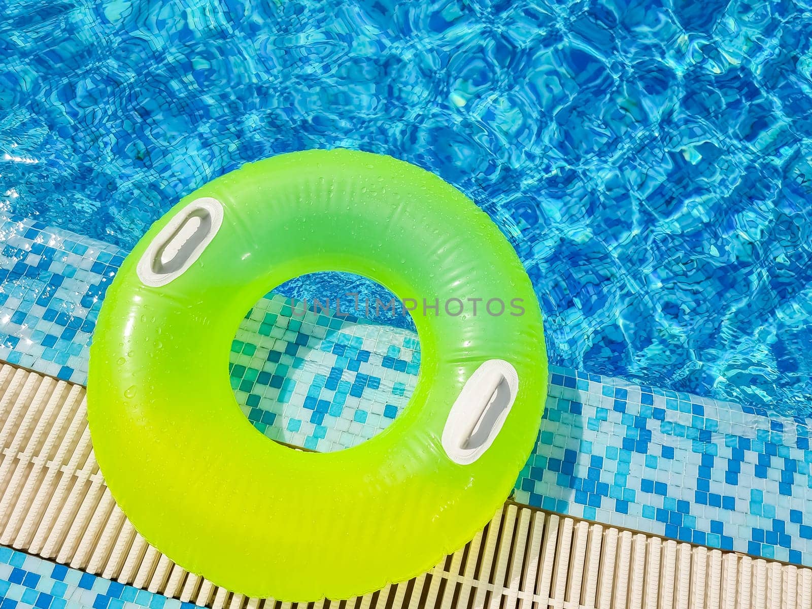 Bright inflatable tube ring floating on blue water surface with splashes in swimming pool during daytime