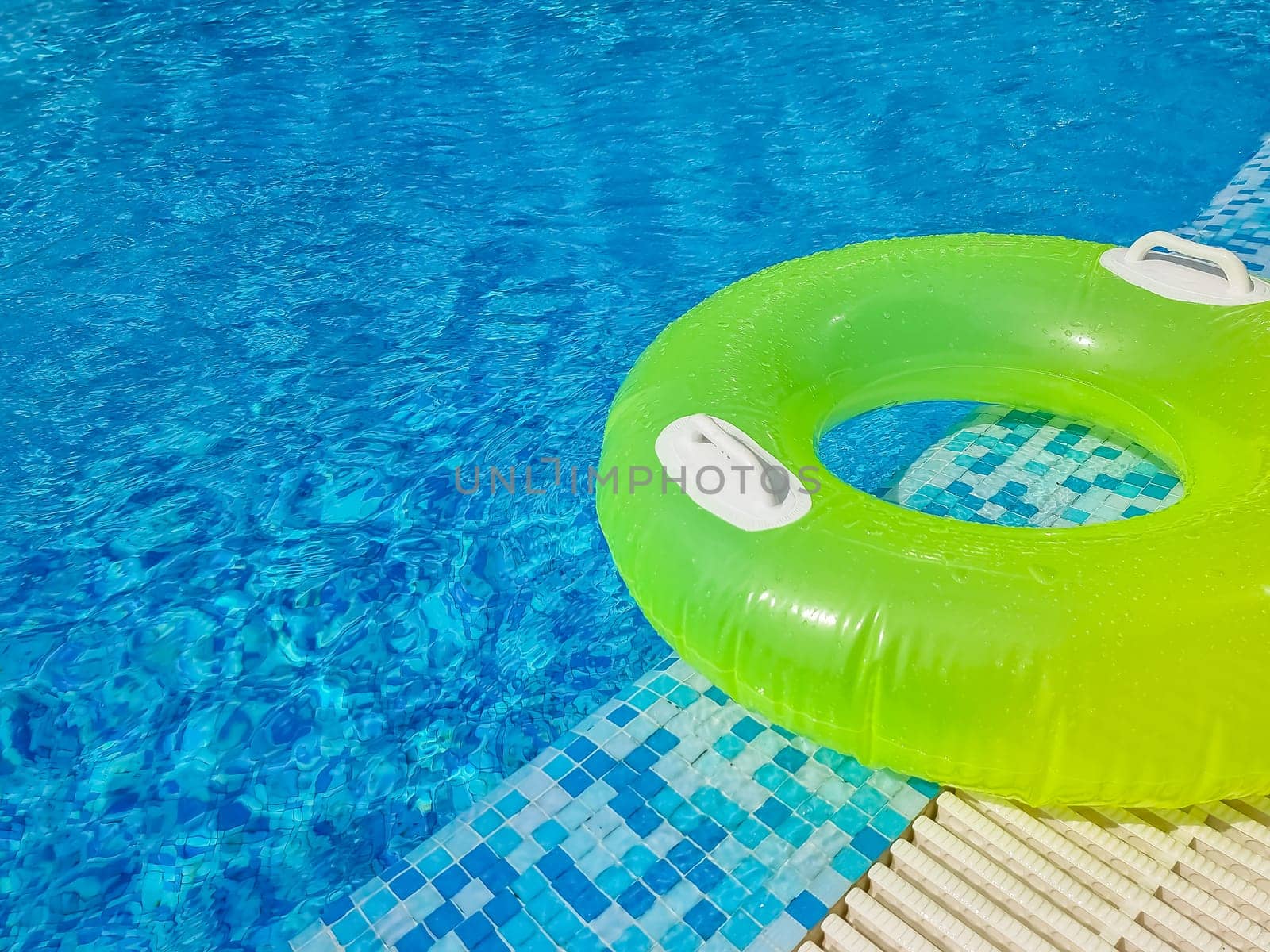 Bright inflatable tube ring floating on blue water surface with splashes in swimming pool during daytime