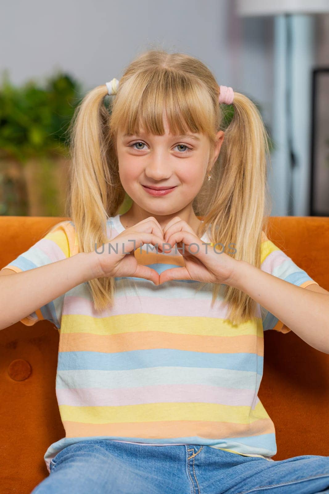 I love you. Child kid girl makes symbol of love, showing heart sign to camera, express romantic feelings, express sincere positive feelings. Charity, gratitude, donation. Female teen at home. Vertical