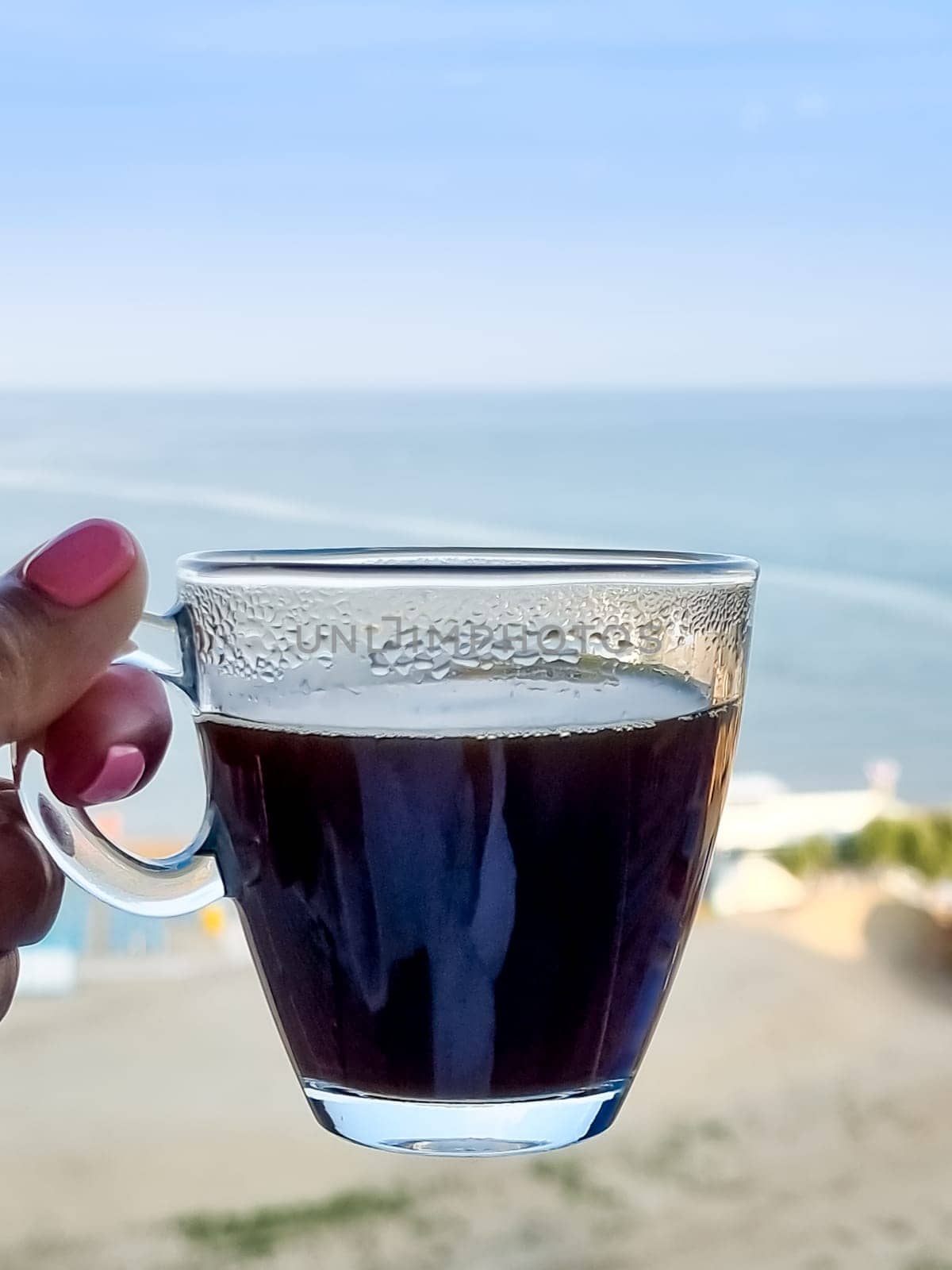 White coffee mug in man hand on terrace overlooking sea or ocean. Enjoying morning coffee on paradise island