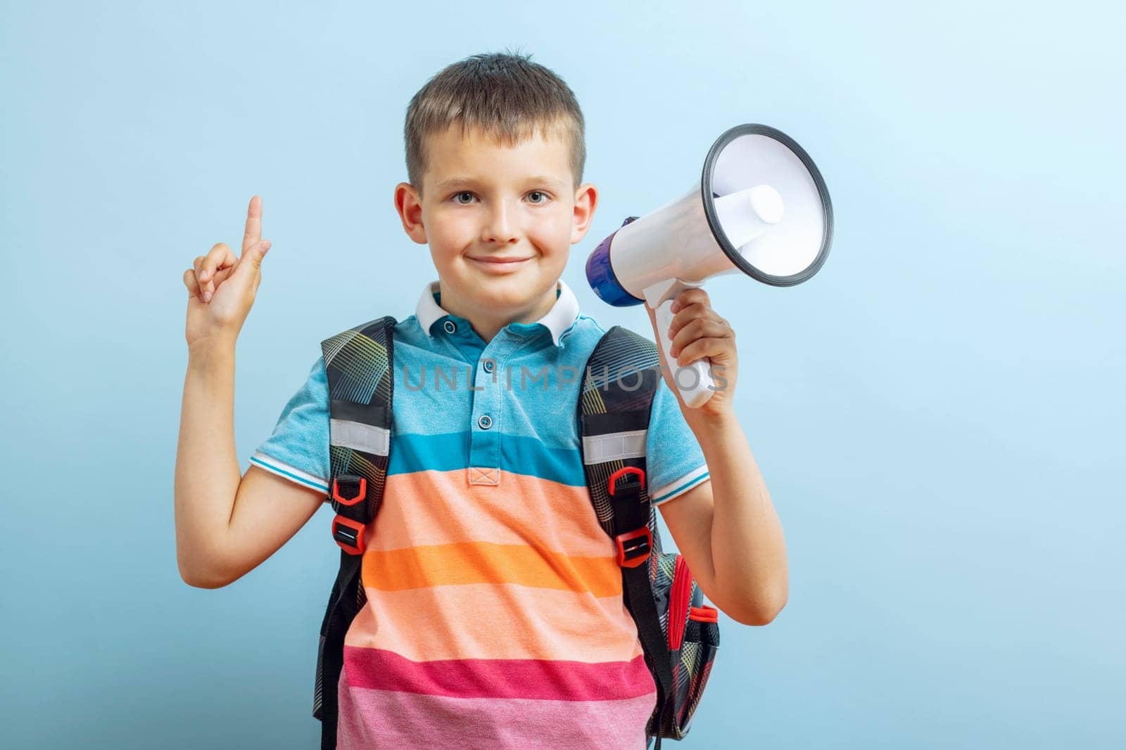 Little school boy shouting through a megaphone on blue background. Boy with megaphone making an announcement