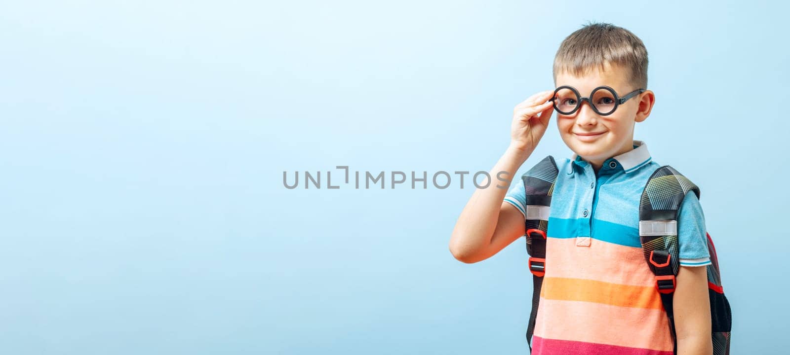 Positive elementary school nerd boy in eyeglasses against blue background.