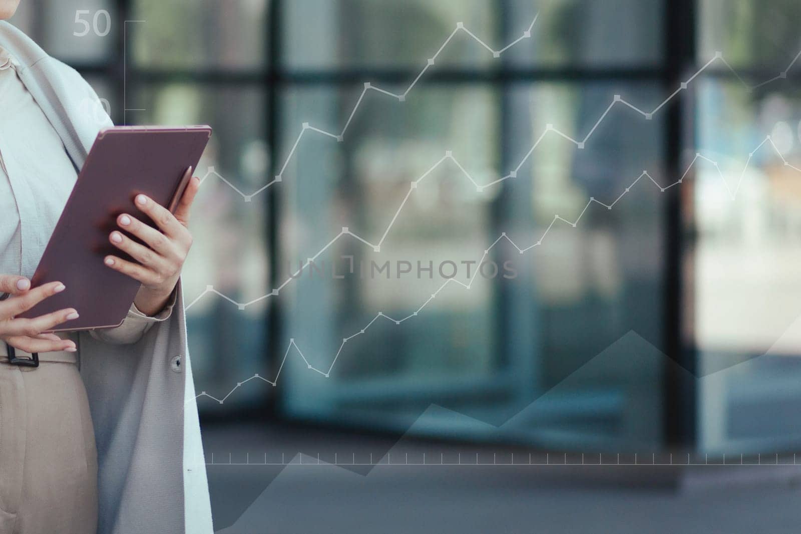 Digital tablet in female hands close-up against the background of an office building and charts growing up. Successful startup concept.