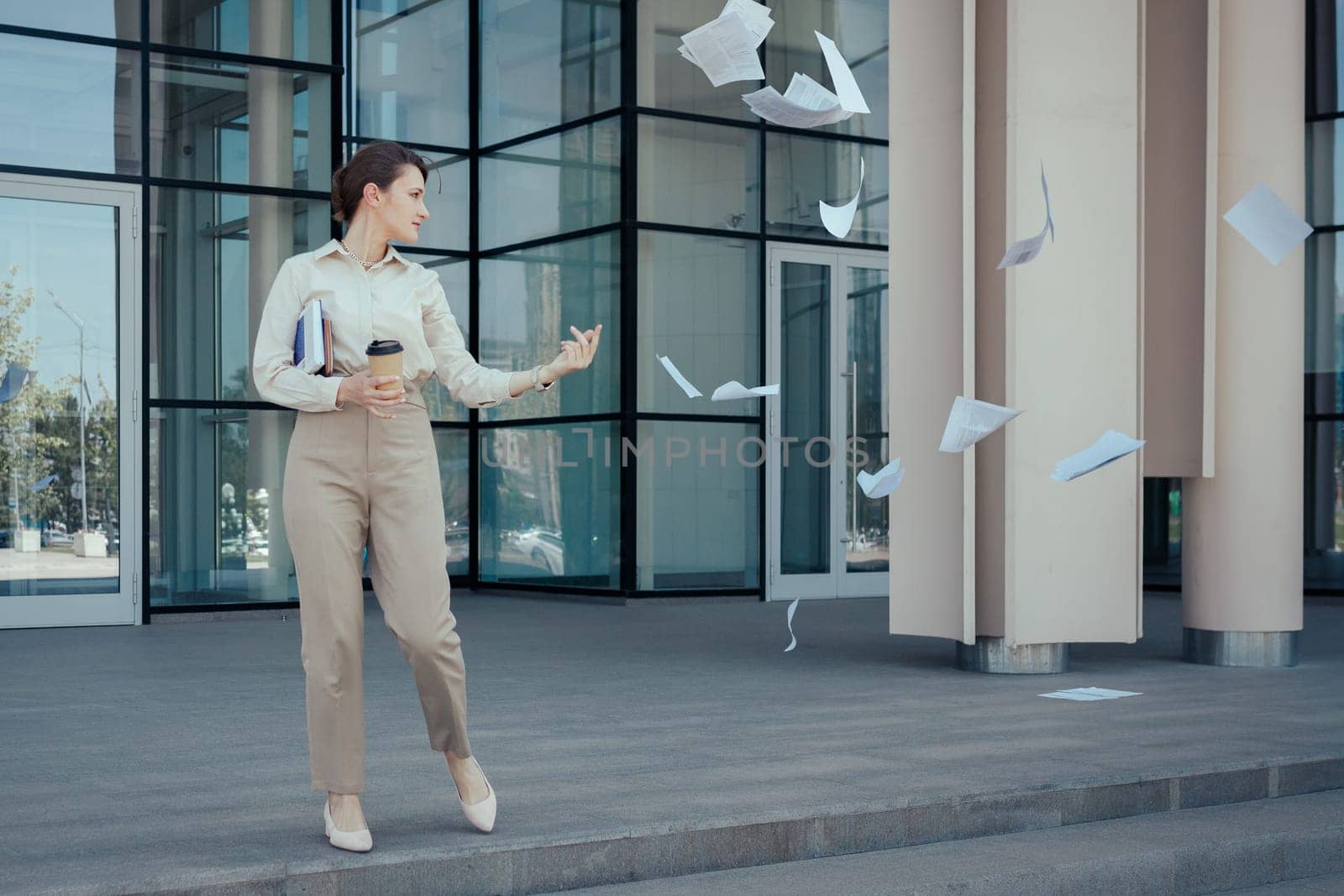 Business woman runs out of an office building throwing paperwork around. How to freeze current affairs before vacation or weekend, time management problems.