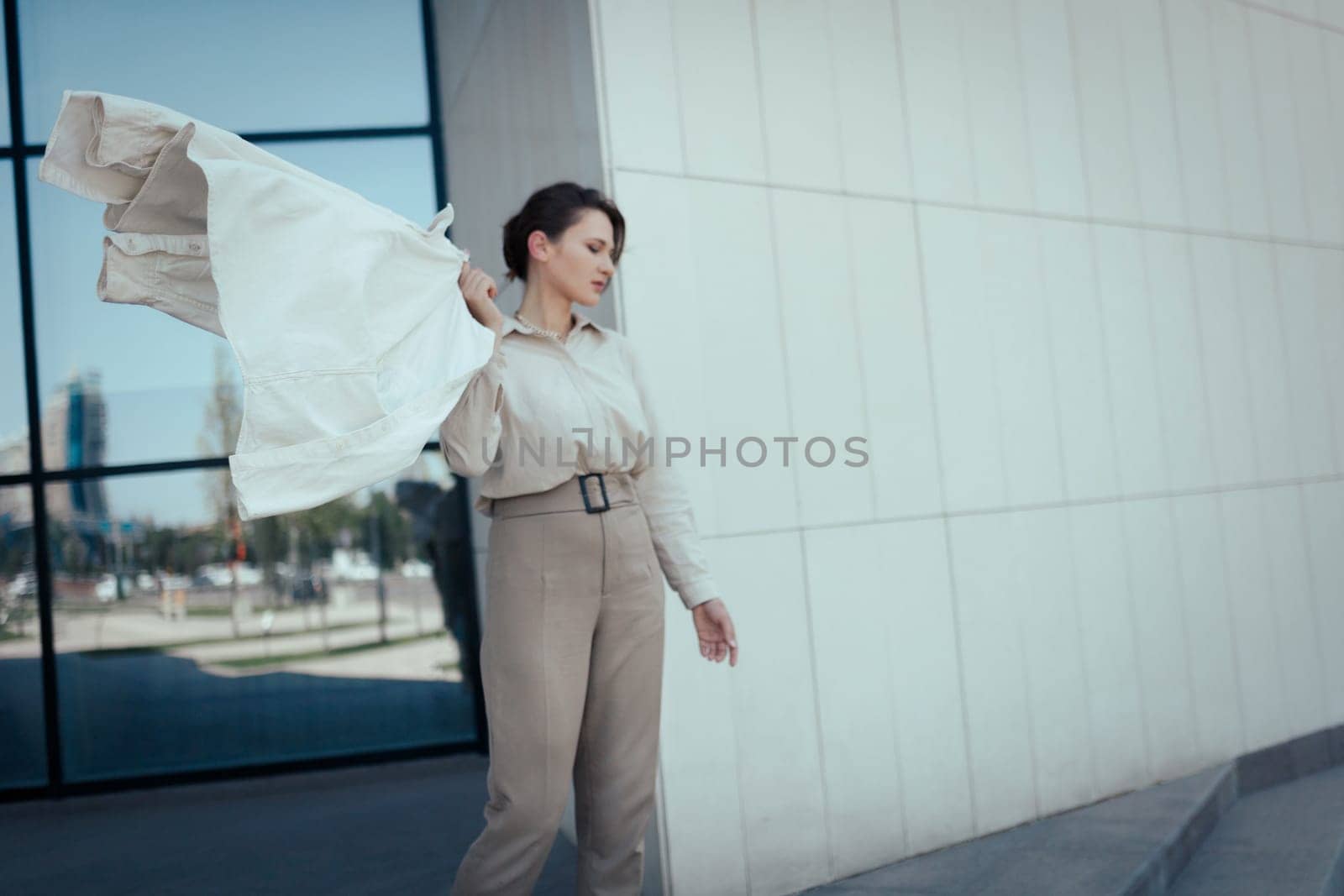 Portrait of a beautiful young successful business woman in beige pant suit standing against office district, copy space.