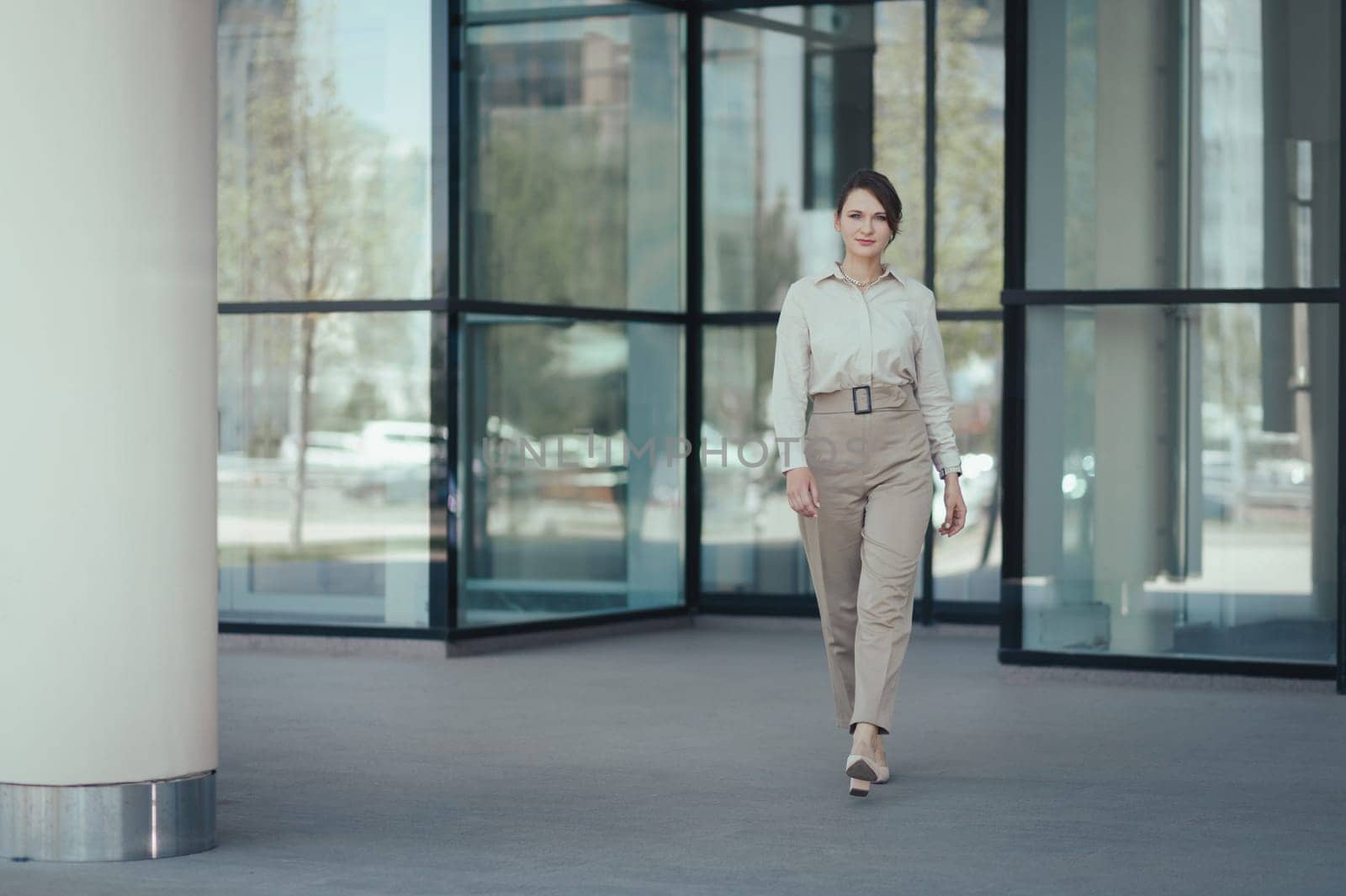 Caucasian attractive business woman in a business suit leaves the office building by Rom4ek