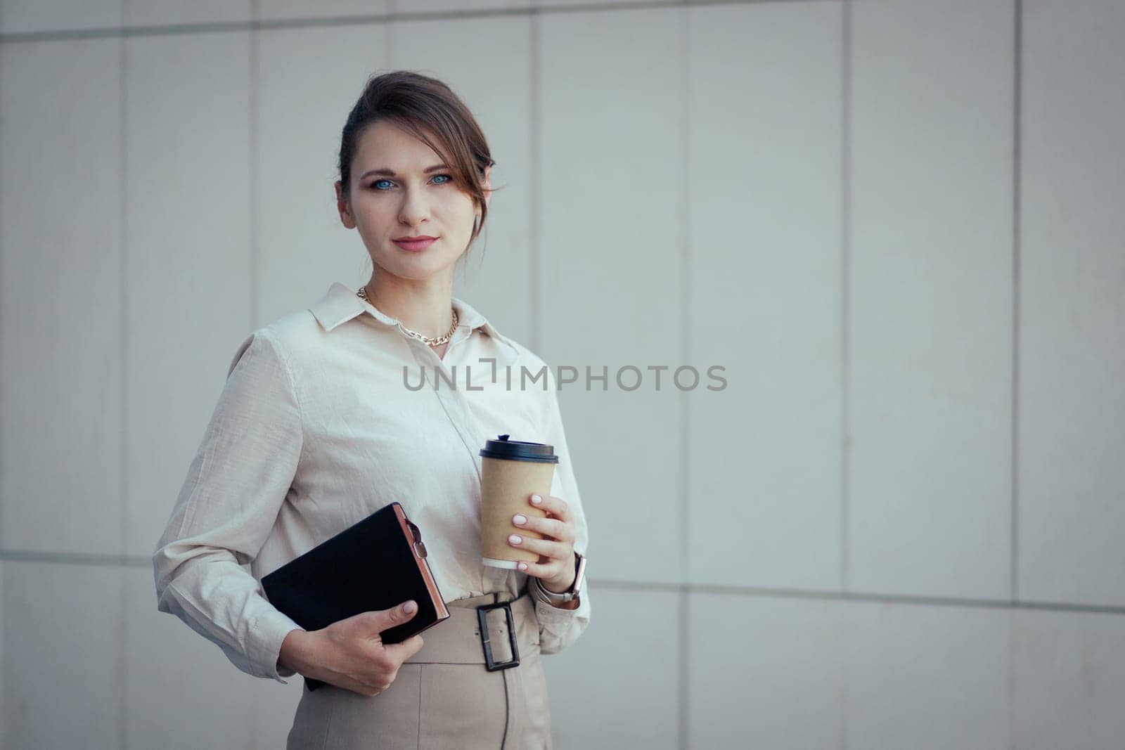 Caucasian young woman in office or business fashion style in clothes with notebook and paper cup with look at camera, copy space.