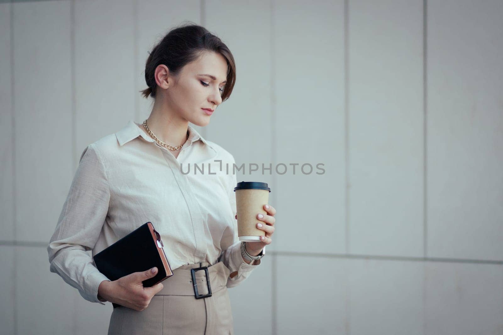 Young caucasian business woman looks sadly at a paper cup because she ran out of coffee, copy space.