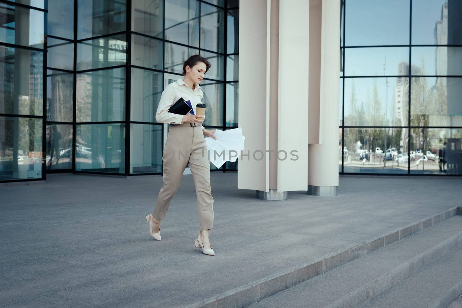 Purposeful business woman with coffee notepad and documents hurry coming out of the office building.