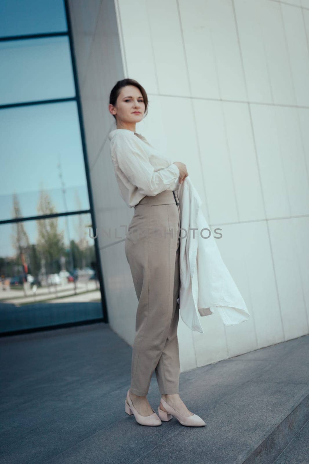 Portrait of a beautiful young business woman standing against office center, vertical.