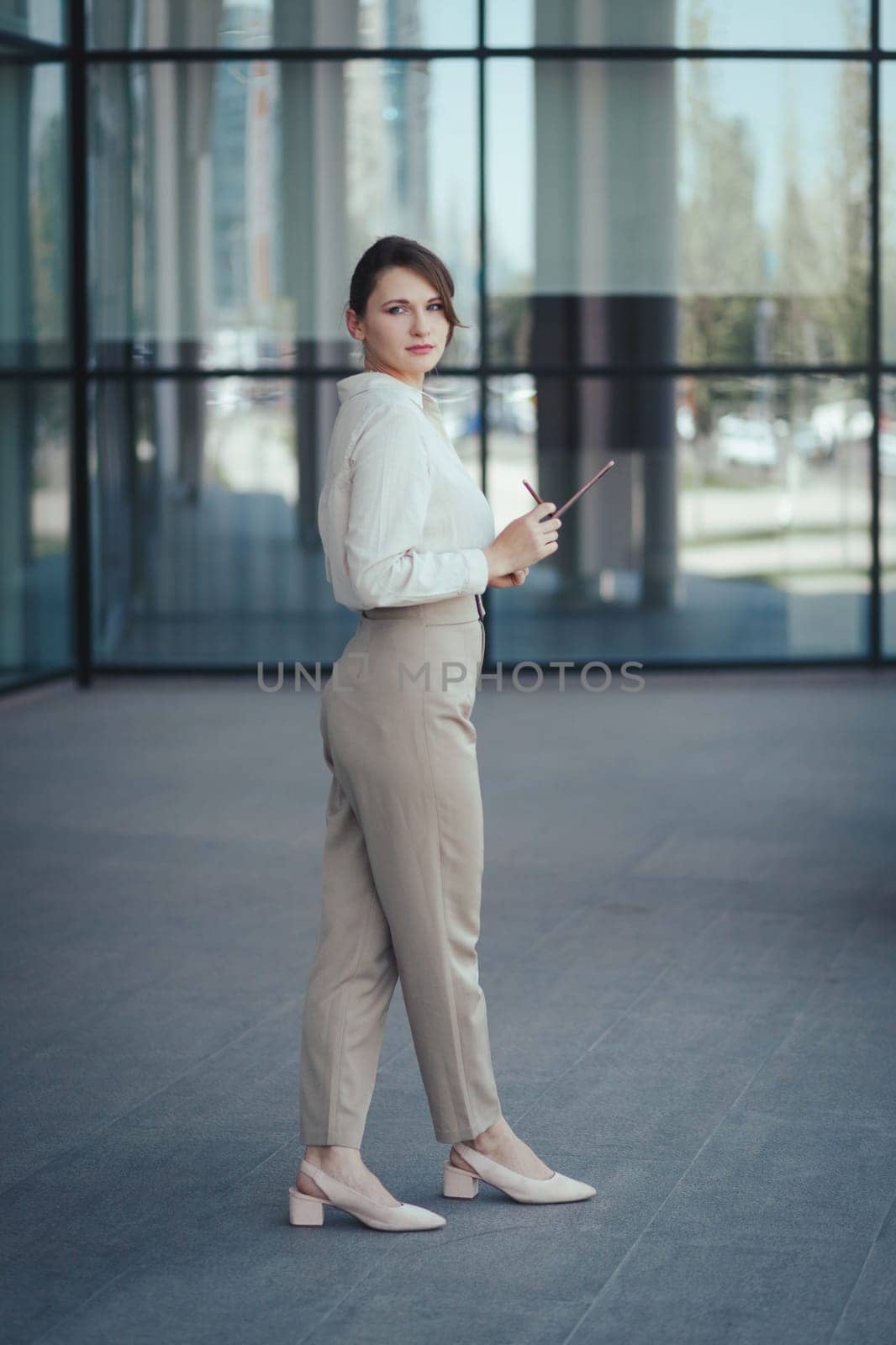 Young caucasian business woman in office or business fashion style pantsuit in beige tones with digital tablet in hands, vertical.