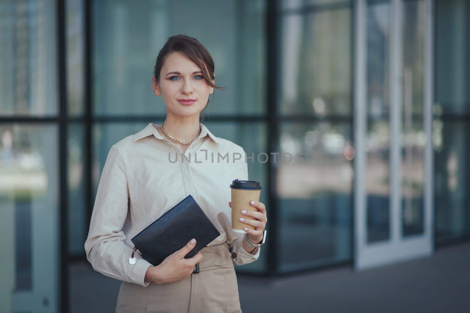 Young caucasian woman left the office for a coffee break with a notepad and coffee in a paper cup.