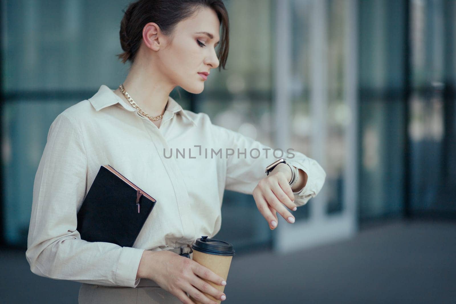 Business woman with a notepad and a paper cup with coffee looks at her watch. The concept of time management in a modern pace.