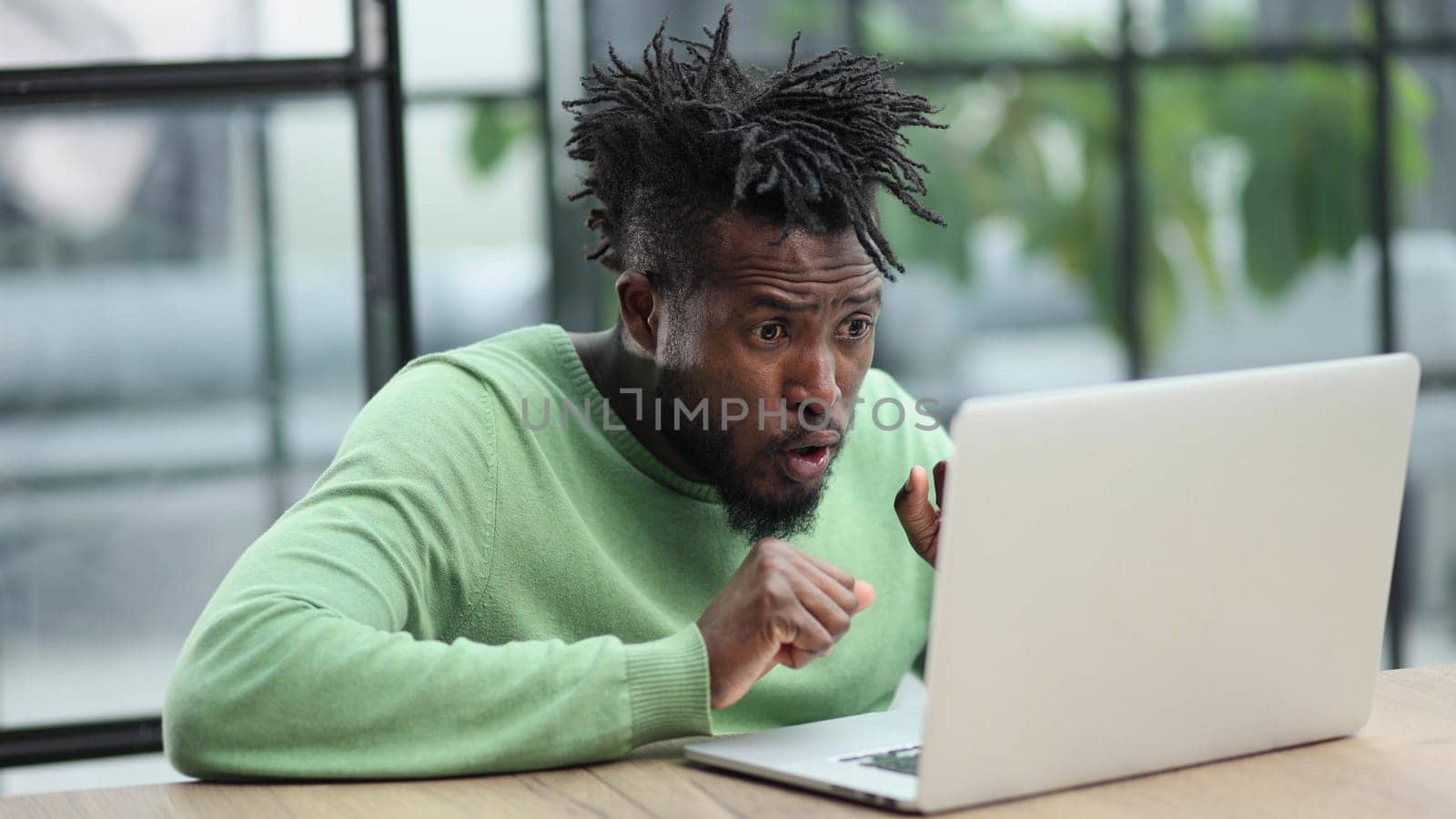 Young african american business man sitting in loft office or cafe, working on new online IT startup project, using laptop by Prosto