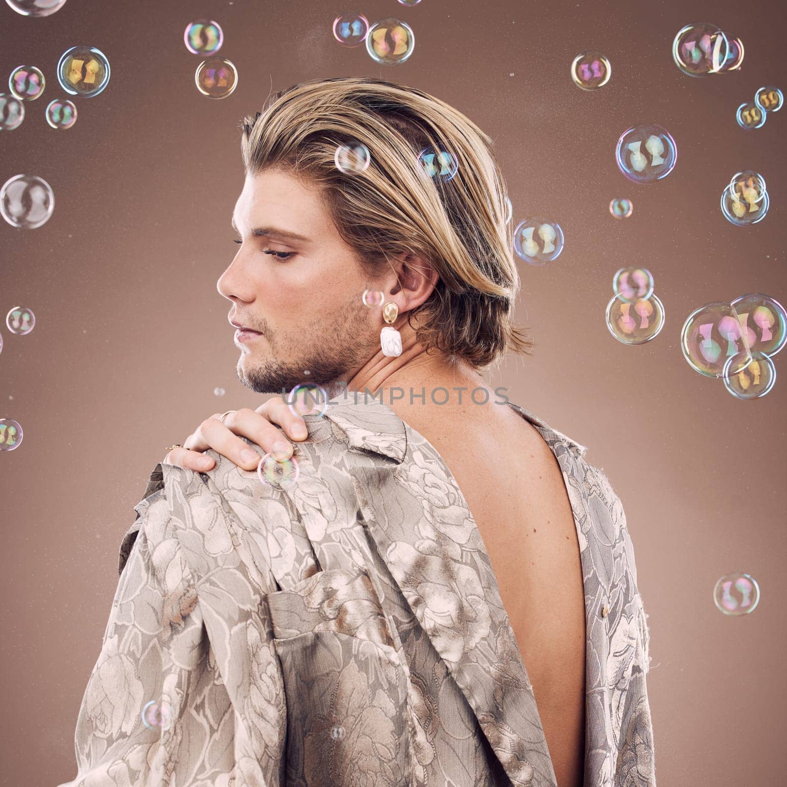 Beauty, lgbtq fashion and man with bubbles in studio on brown background for cosmetics, style and modern outfit. Creative art, luxury design and non binary model with soap bubbles, jewelry and makeup by YuriArcurs