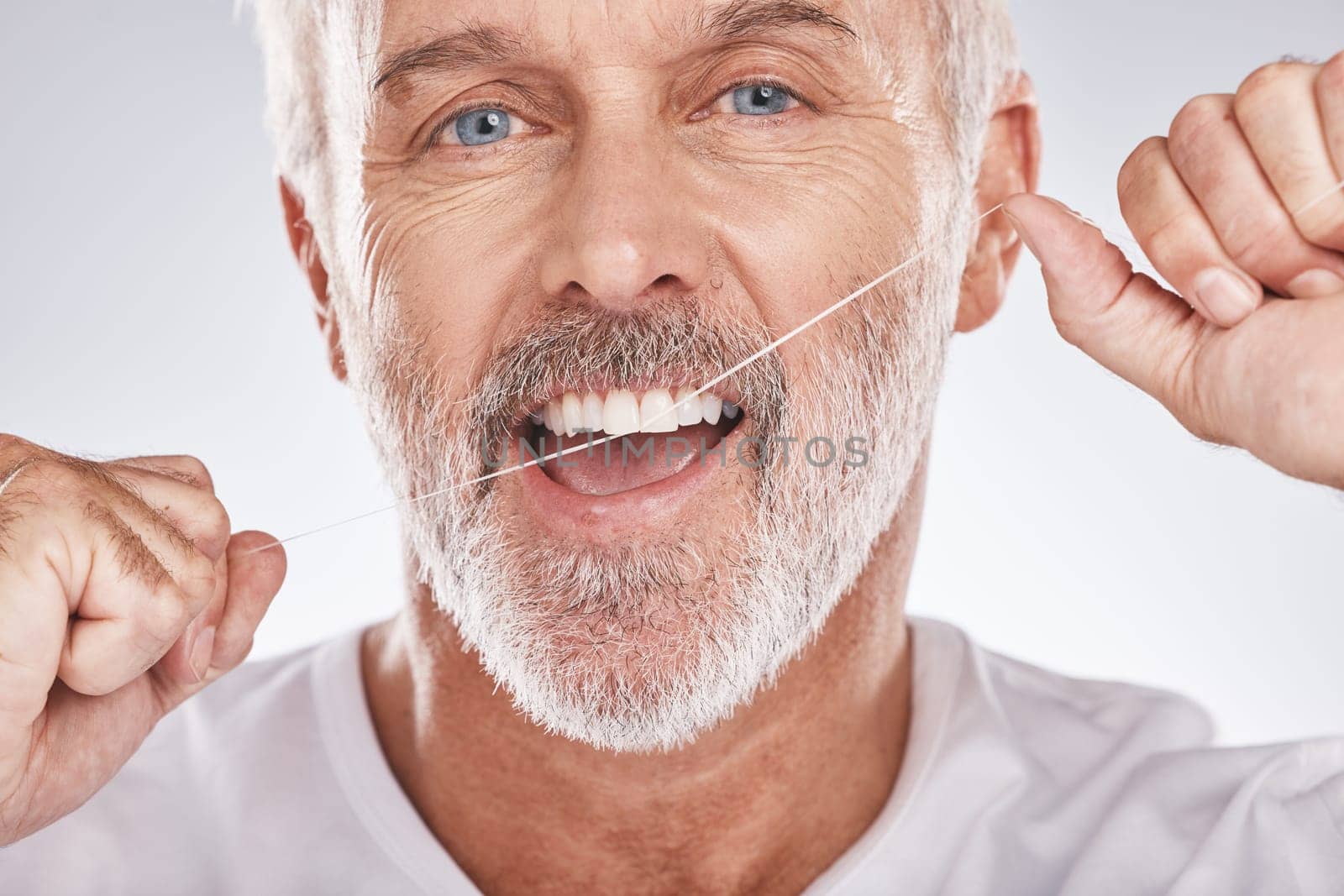 Dental, floss and face of senior man in studio isolated on a gray background. Portrait, cleaning or elderly male model with product flossing teeth for oral wellness, healthy gum hygiene or tooth care.