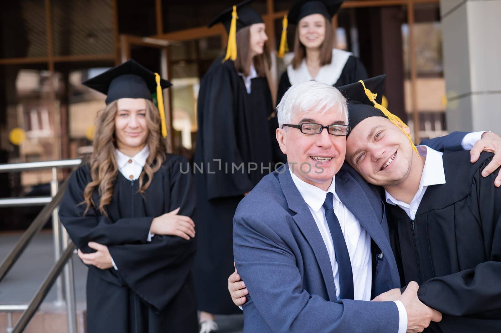 A gray-haired male teacher congratulates students on their graduation from the university. by mrwed54
