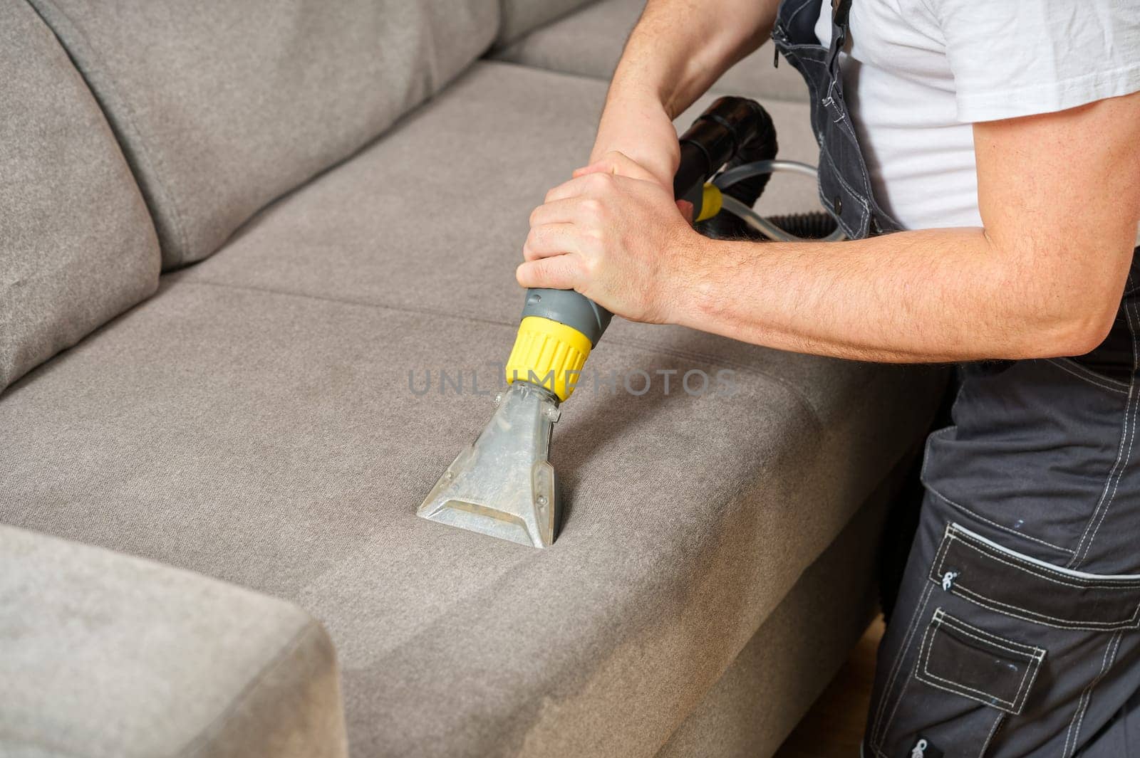 Dry cleaner's man employee removing dirt from textile furniture in flat. closeup, vacuum clean sofa by PhotoTime
