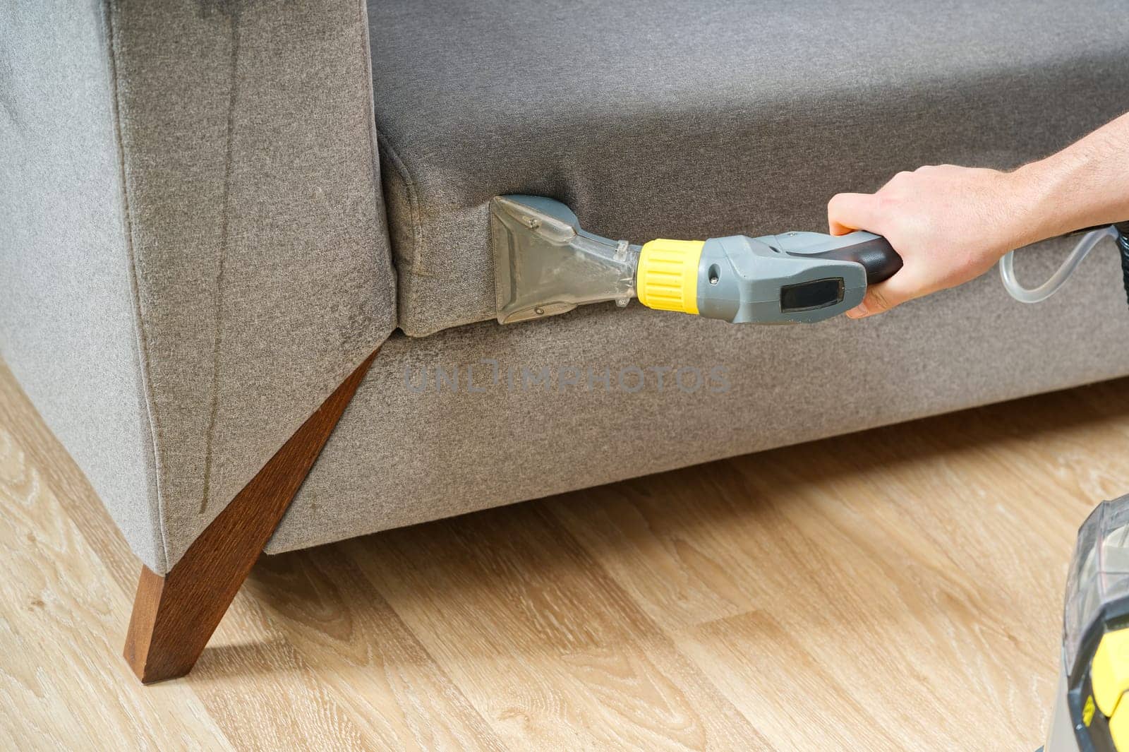 Dry cleaner's man employee removing dirt from textile furniture in flat. closeup, vacuum clean sofa by PhotoTime