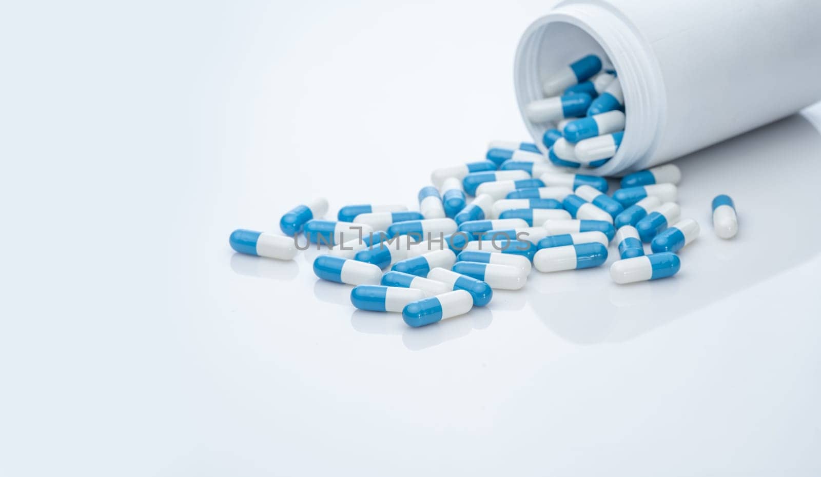 Blue-white antibiotic capsule pills spread out of plastic drug bottles. Antibiotic drug resistance. Prescription drugs. Healthcare and medicine. Pharmaceutical industry. Pharmacy product. Medication.