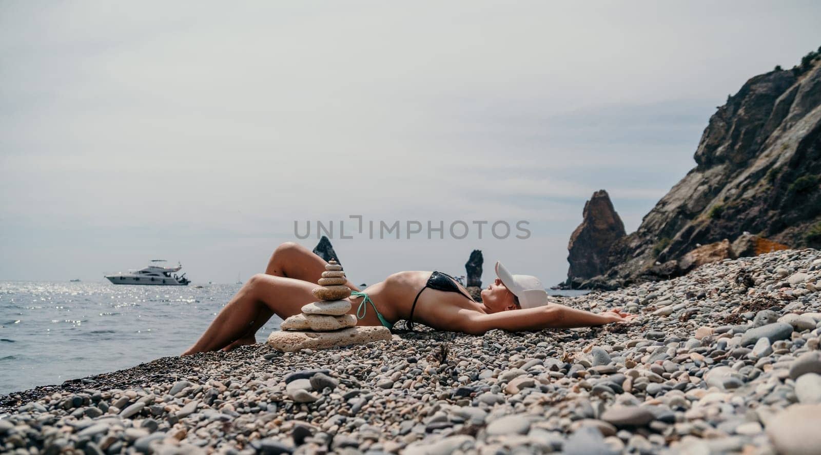Woman bilds stones pyramid on the seashore on a sunny day on the blue sea background. Happy holidays. Pebble beach, calm sea, travel destination. Concept of happy vacation on the sea, meditation, spa