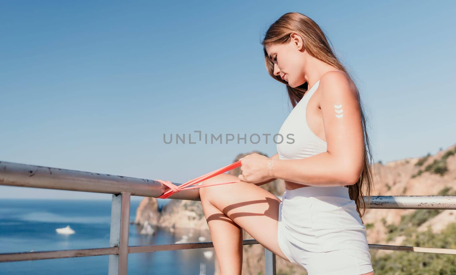 Woman sea fitness. Happy woman with long hair, fitness instructor in white doing stretching and pilates with ribbons in park near the sea. Female fitness yoga routine concept. Healthy lifestyle. by panophotograph
