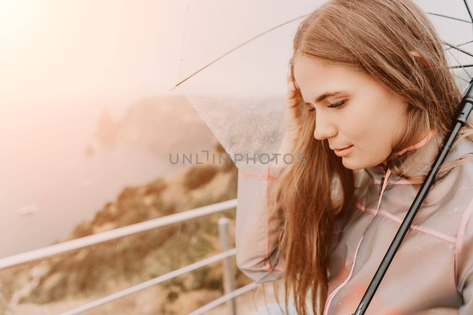 Woman rain park. Happy woman portrait wearing a raincoat with transparent umbrella outdoors on rainy day in park near sea. Girl on the nature on rainy overcast day