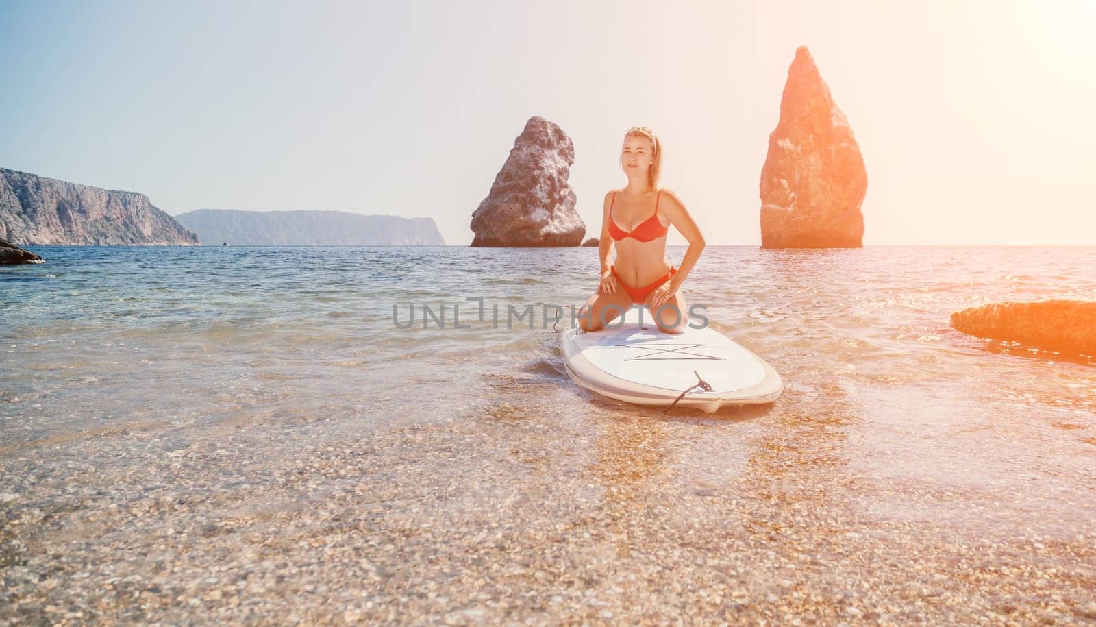 Close up shot of beautiful young caucasian woman with black hair and freckles looking at camera and smiling. Cute woman portrait in a pink bikini posing on a volcanic rock high above the sea