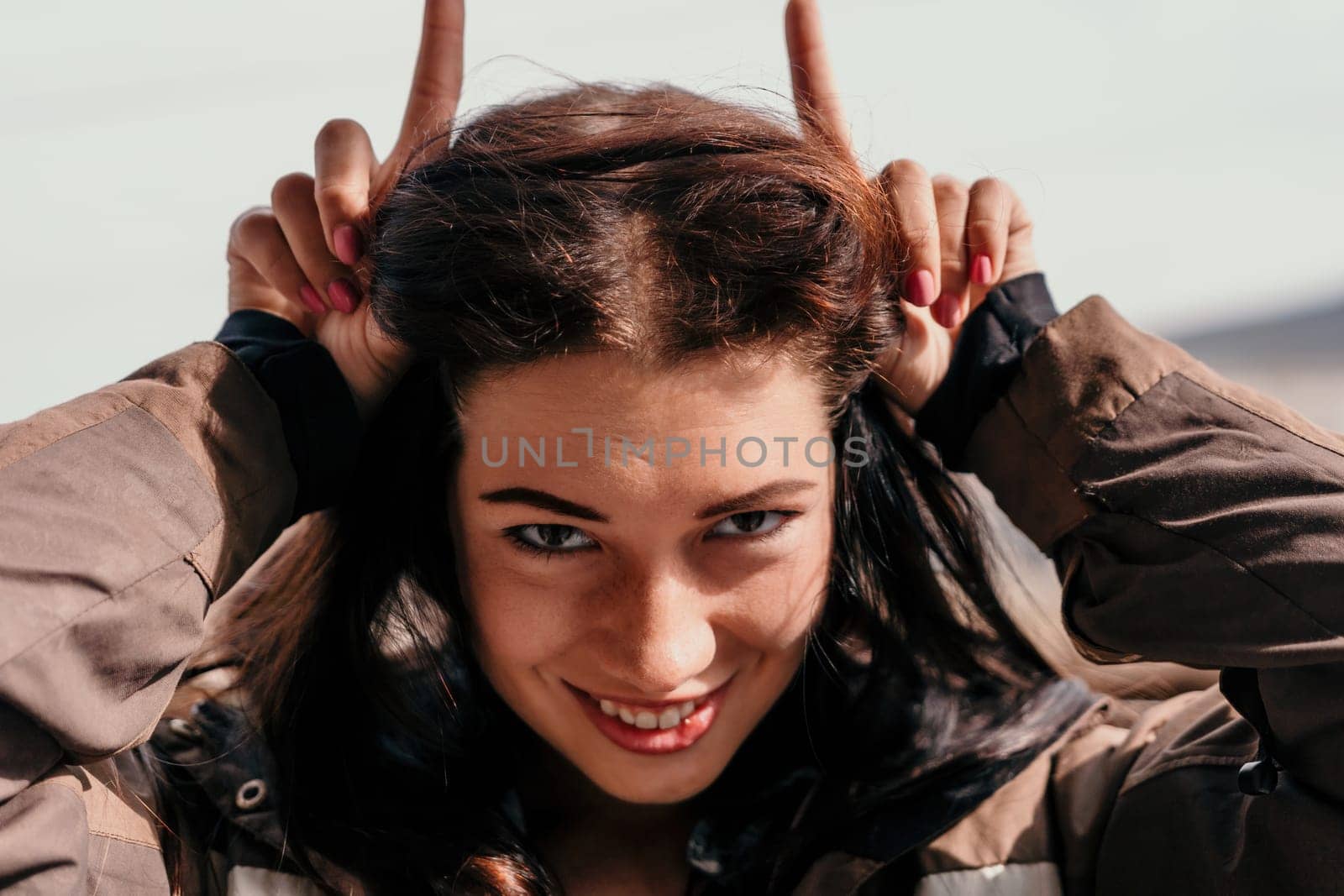 Happy young smiling woman with freckles outdoors portrait. Soft sunny colors. Outdoor close-up portrait of a young brunette woman and looking to the camera, posing against autumn nature background by panophotograph