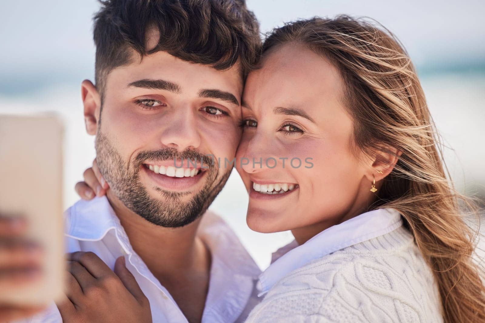 Selfie, love and couple on a date at the beach for valentines day, romance or anniversary in summer. Happiness, smile and young man and woman hugging while taking picture by the ocean on vacation