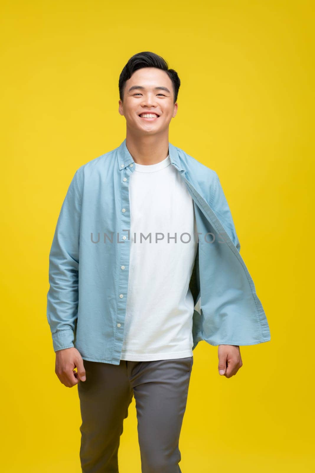 Very handsome casual man smiling and standing on yellow background