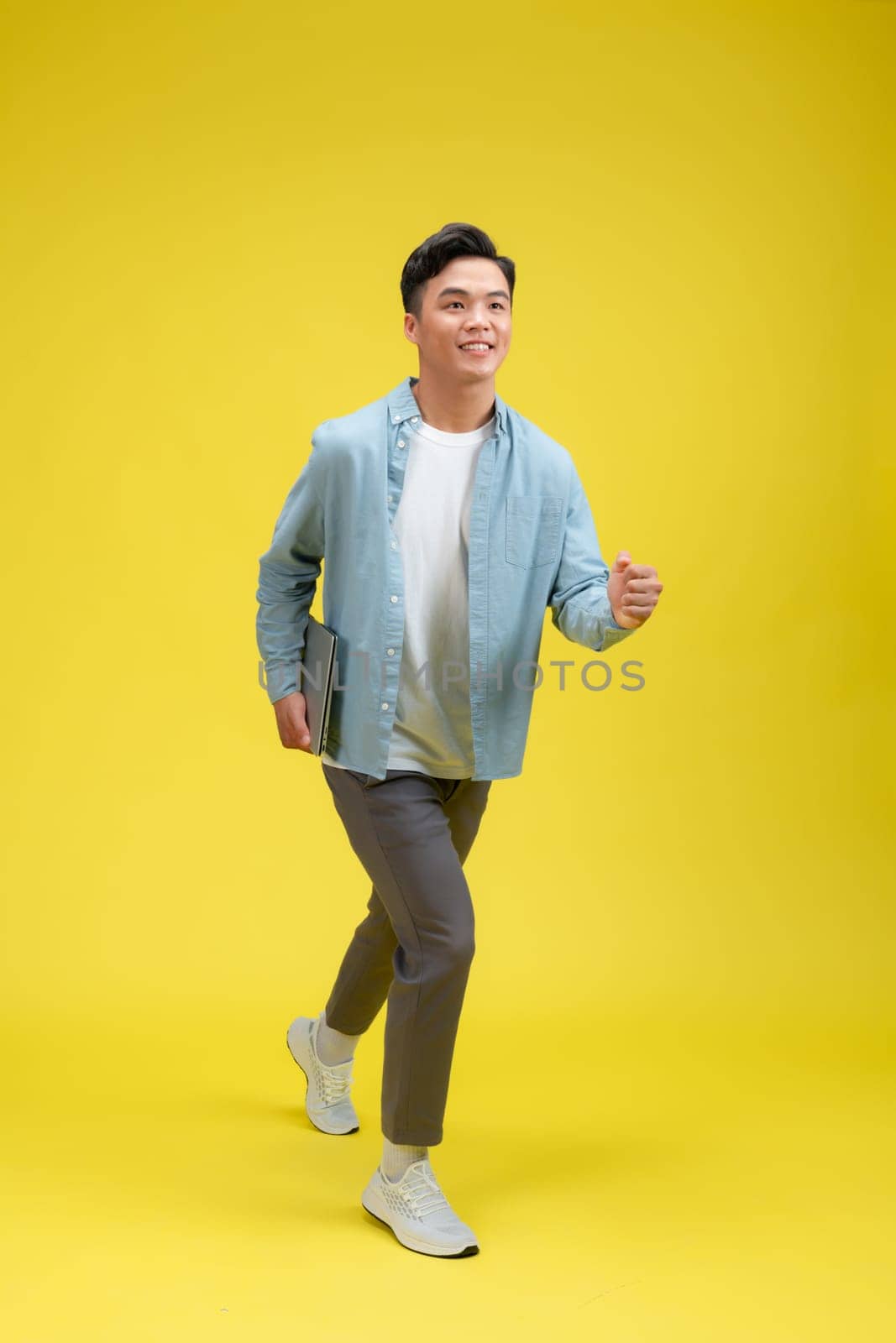 Portrait of young man holding laptop, studio shot on yellow background