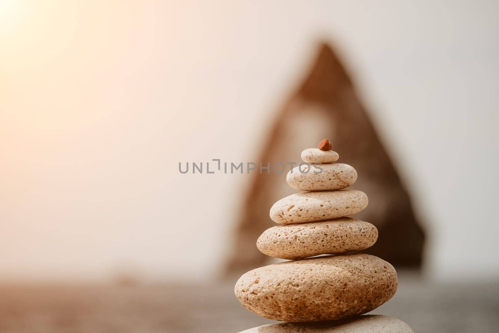 Pyramid stones on the seashore with warm sunset on the sea background. Happy holidays. Pebble beach, calm sea, travel destination. Concept of happy vacation on the sea, meditation, spa, calmness by panophotograph