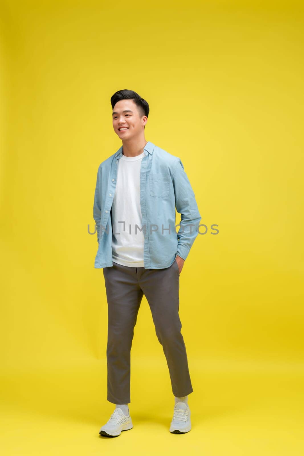 young pretty asian man posing in fashion style on light yellow background, lifestyle people concept