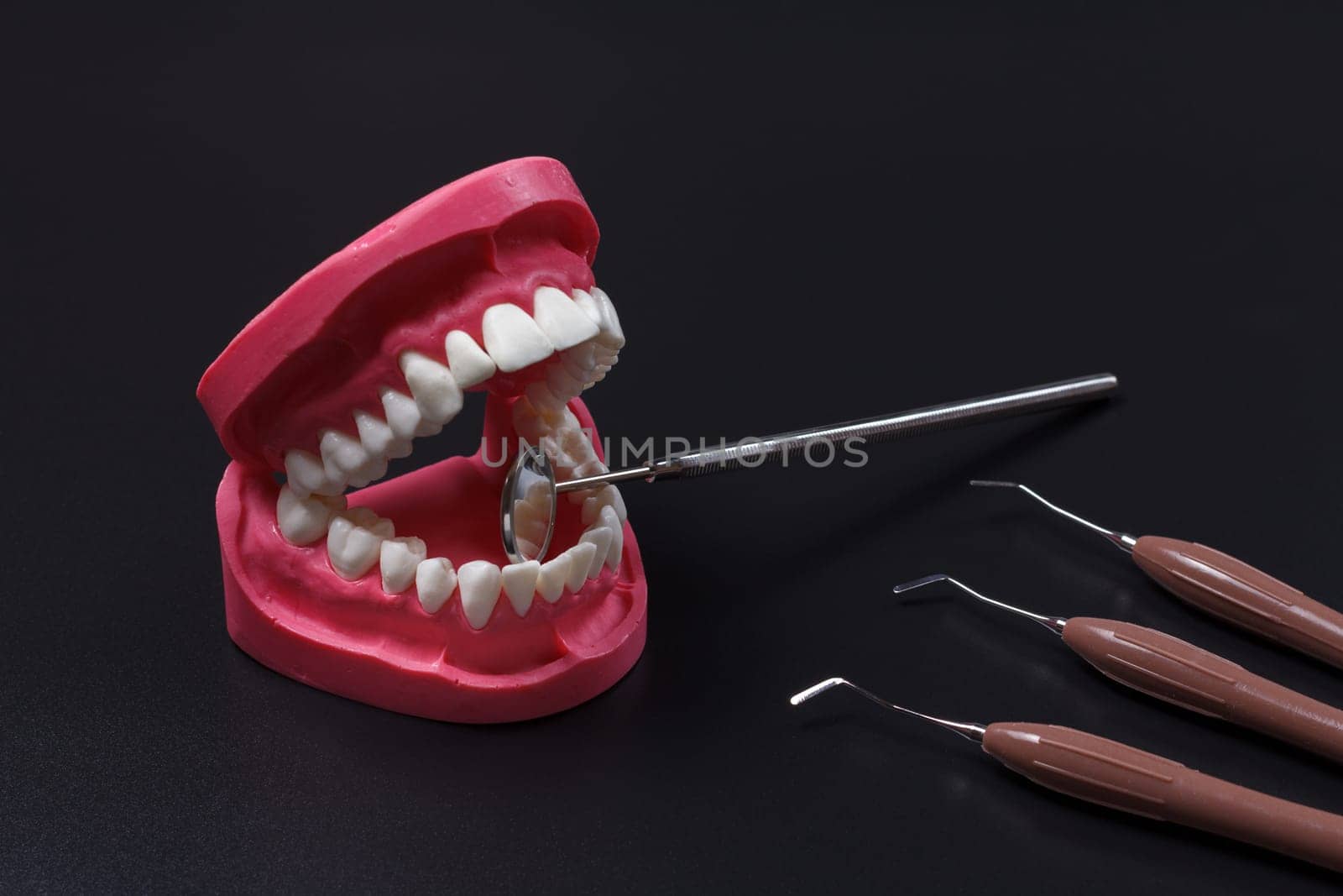 Layout of the human jaw with the mouth mirror and the dental restoration instruments on the black background. Medical tools.