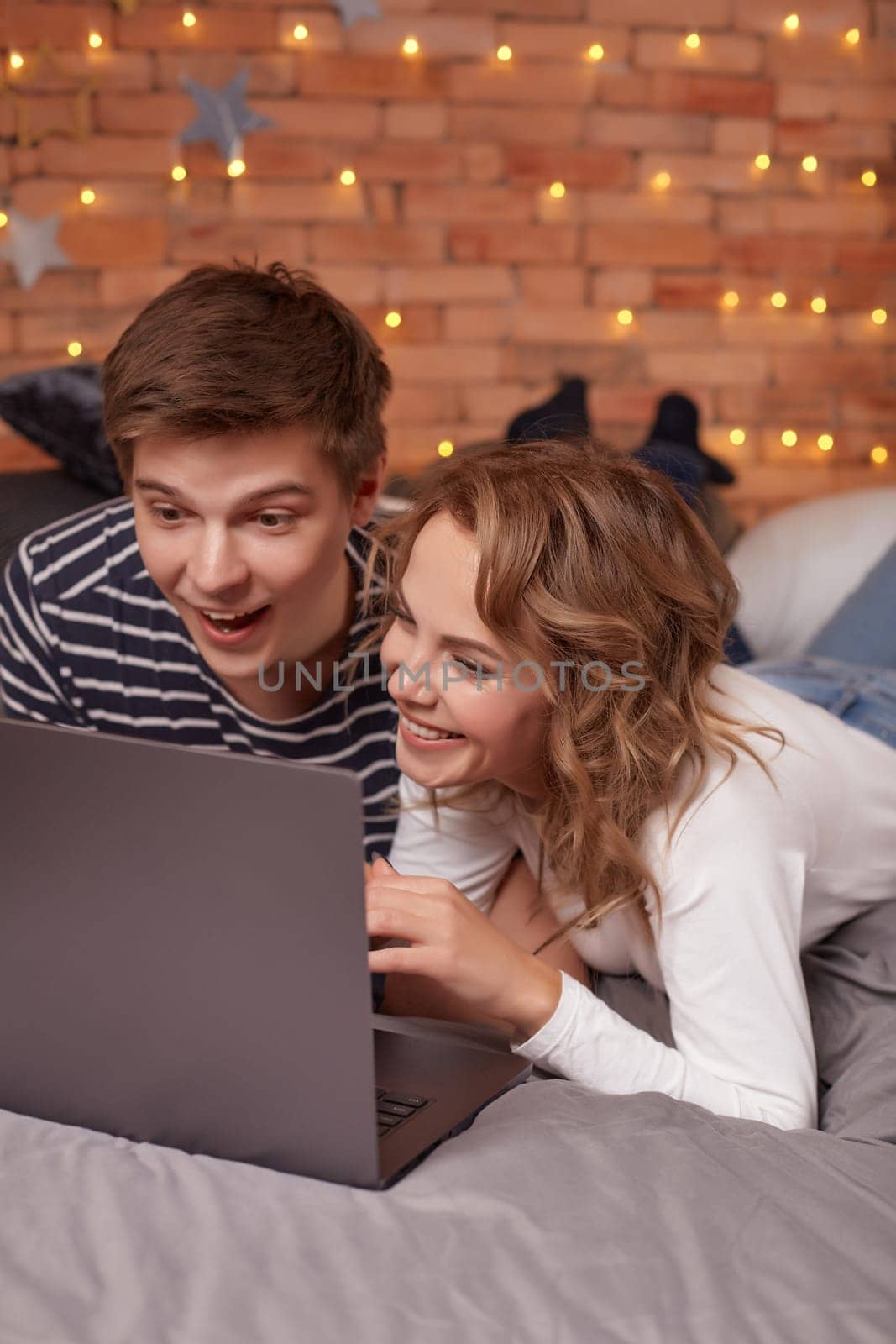 Smiling young couple man and woman lying in bed and watching something on the laptop by nazarovsergey