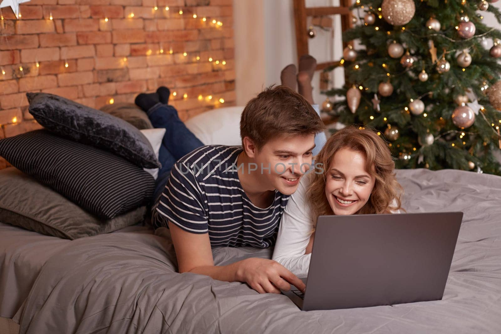 Smiling young couple man and woman lying in bed and watching something on the laptop by nazarovsergey