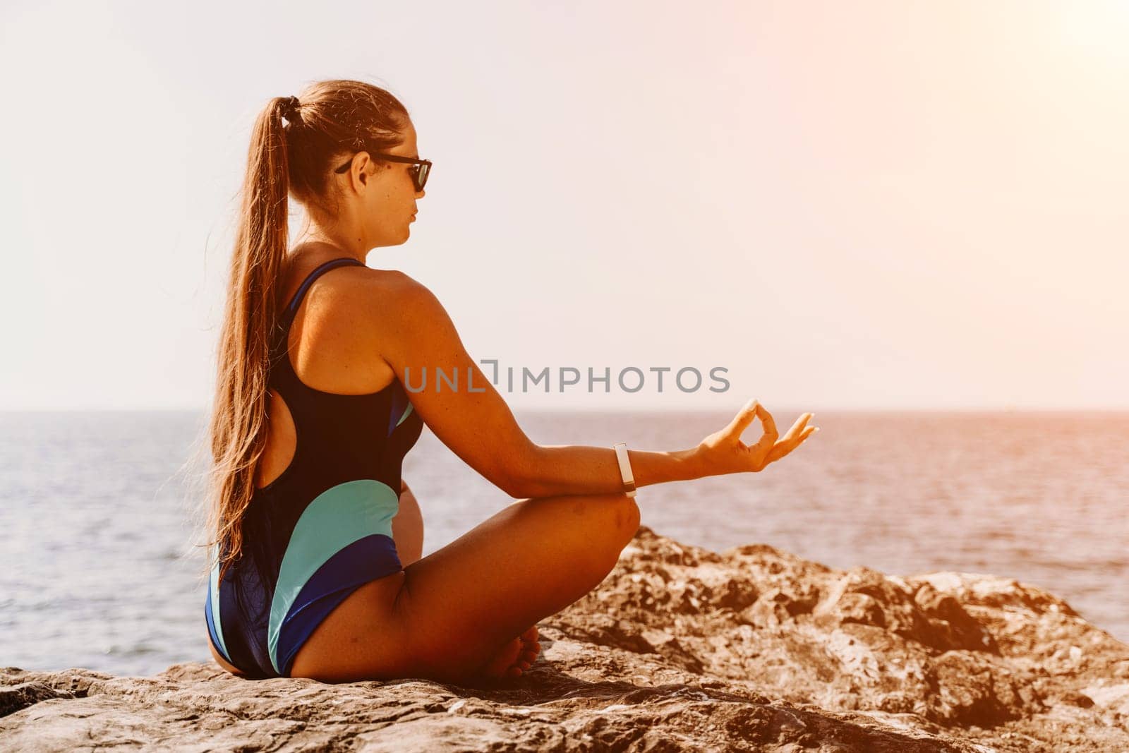 Yoga on the beach. A happy woman meditating in a yoga pose on the beach, surrounded by the ocean and rock mountains, promoting a healthy lifestyle outdoors in nature, and inspiring fitness concept. by Matiunina