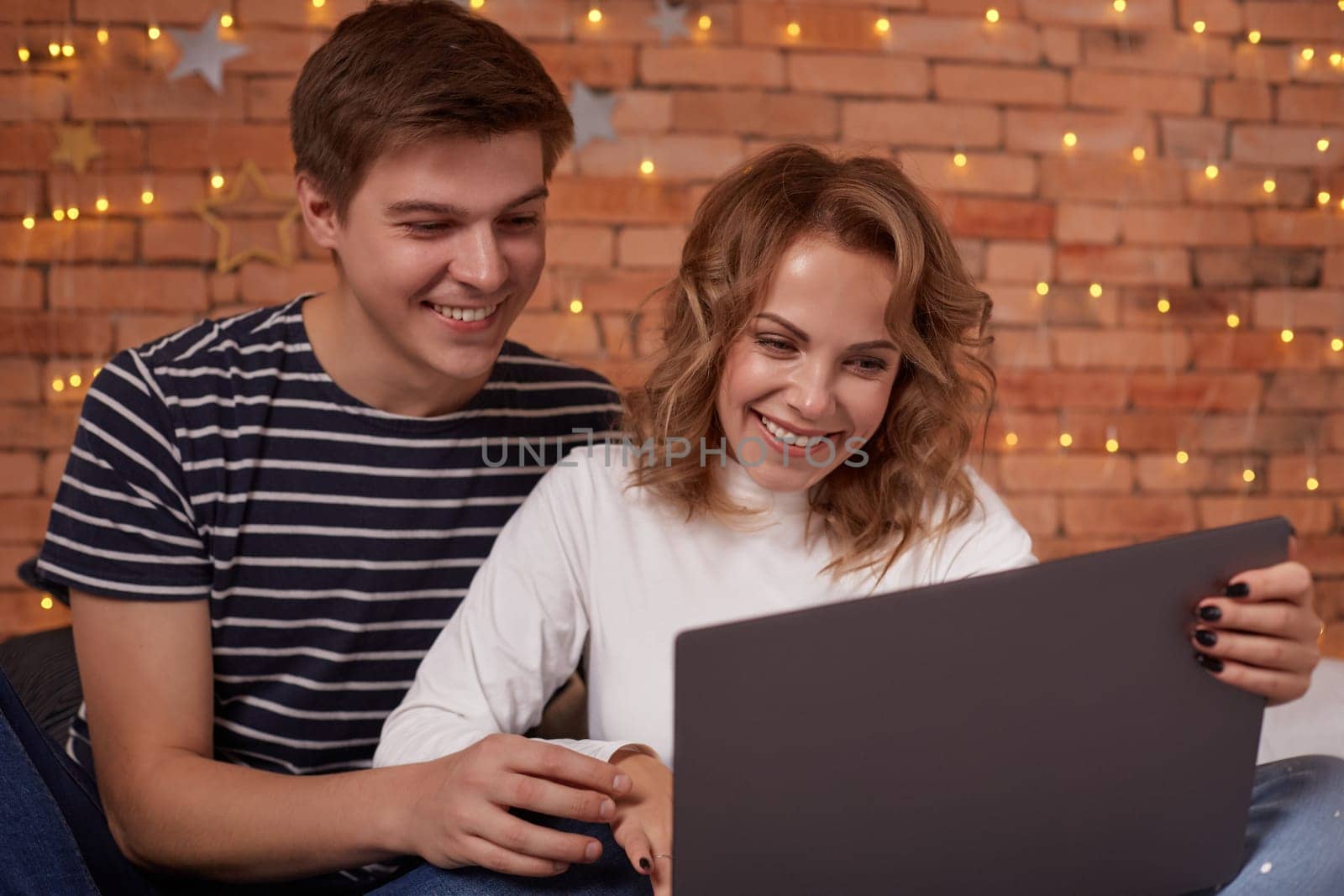 Smiling young couple man and woman sitting on bed and using their laptop by nazarovsergey