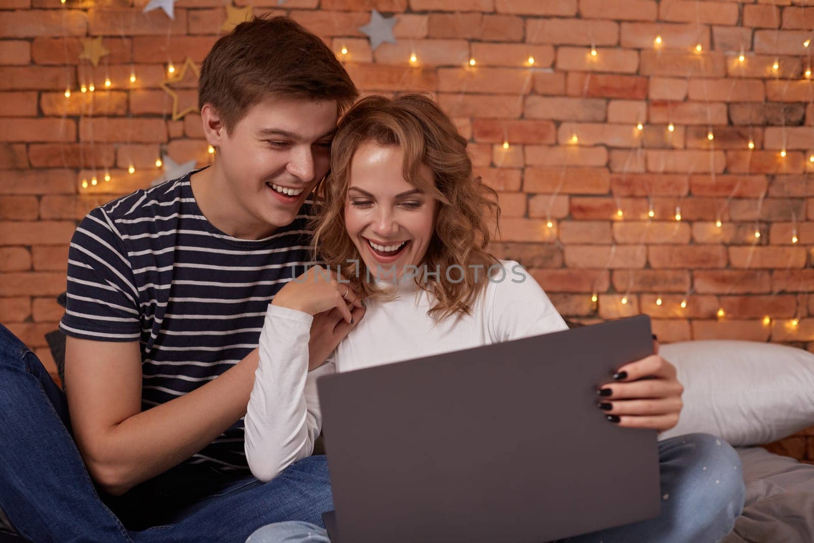 Smiling young couple man and woman sitting on bed and using their laptop by nazarovsergey