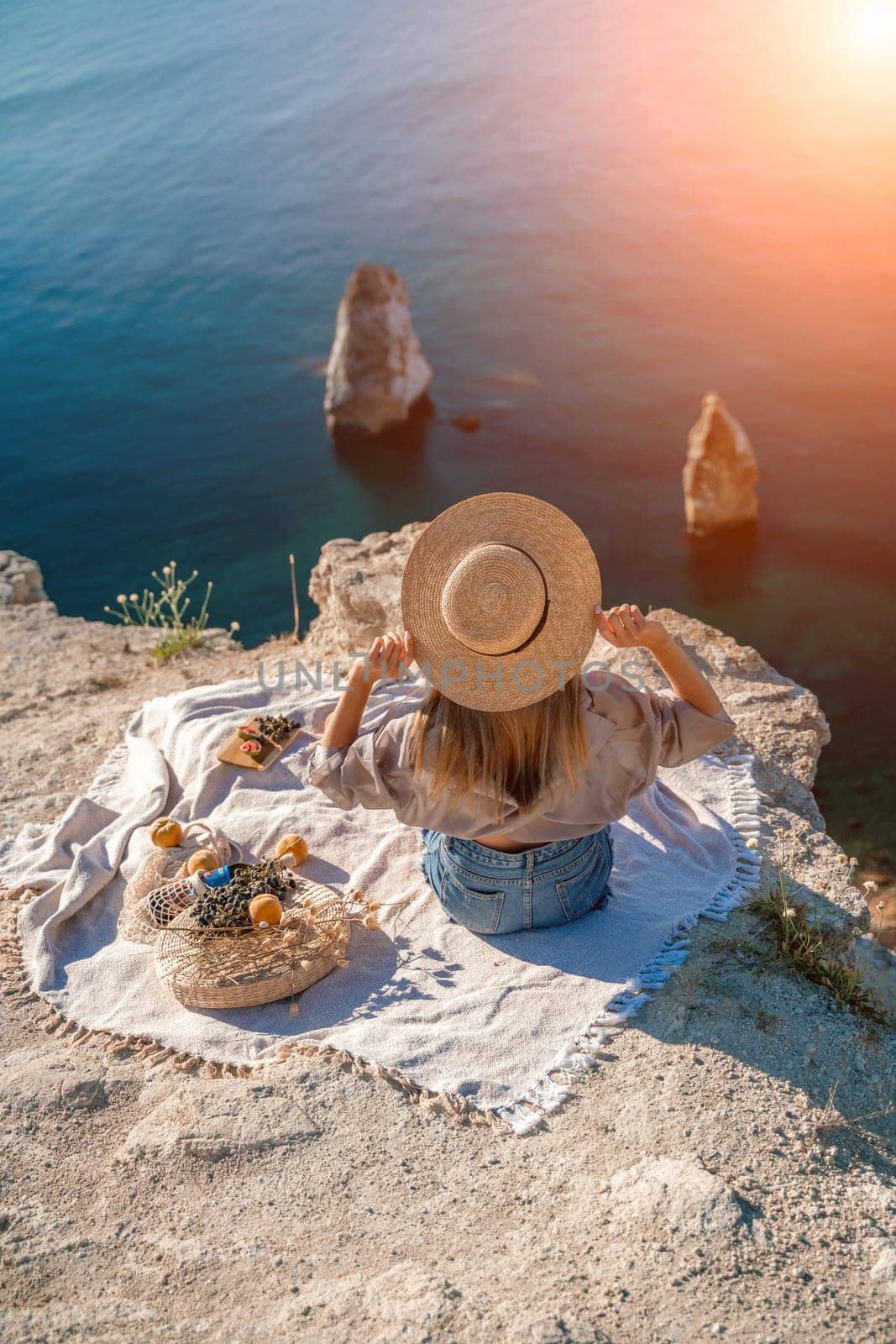 woman sea travel. photo of a beautiful woman with long blond hair in a pink shirt and denim shorts and a hat having a picnic on a hill overlooking the sea by Matiunina