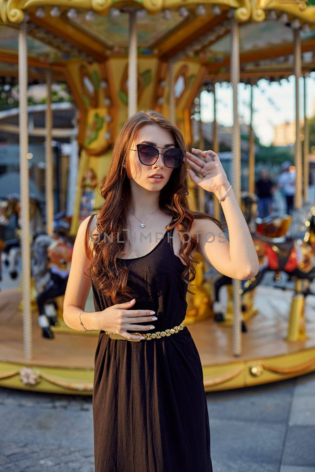 Portrait of a beautiful brunette woman in evening dress next to a children's carousel. by nazarovsergey