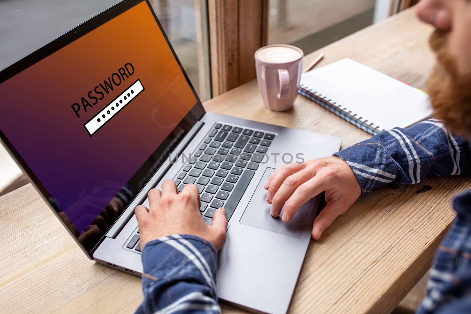 Cropped image of a young man working on his laptop in a coffee shop, young male student enters a password on computer sitting at wooden table. by nazarovsergey