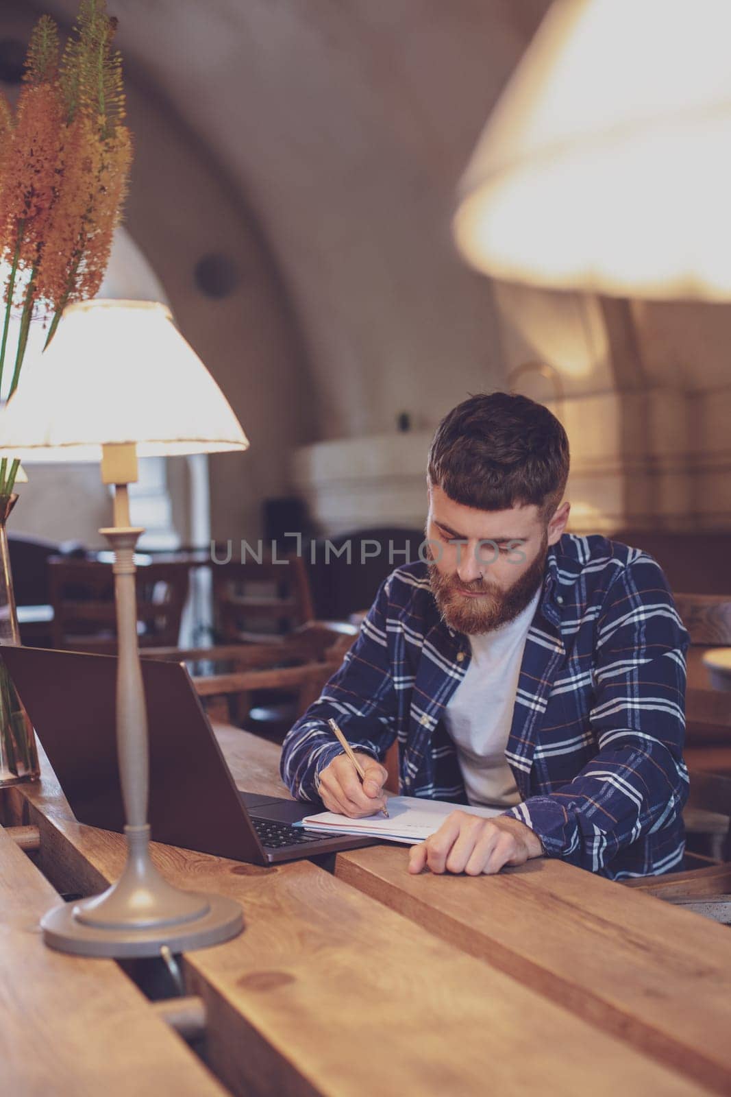 Casual business man or freelancer planning his work on notebook, working on laptop computer with smart phone, cup of coffee on table at coffee shop or home office, working from cafe concept