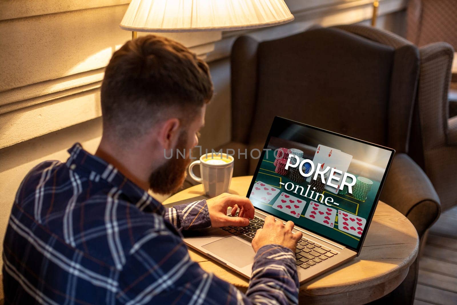 Young man playing poker via netbook during work-break in coffee shop, male sitting in front open laptop computer. by nazarovsergey