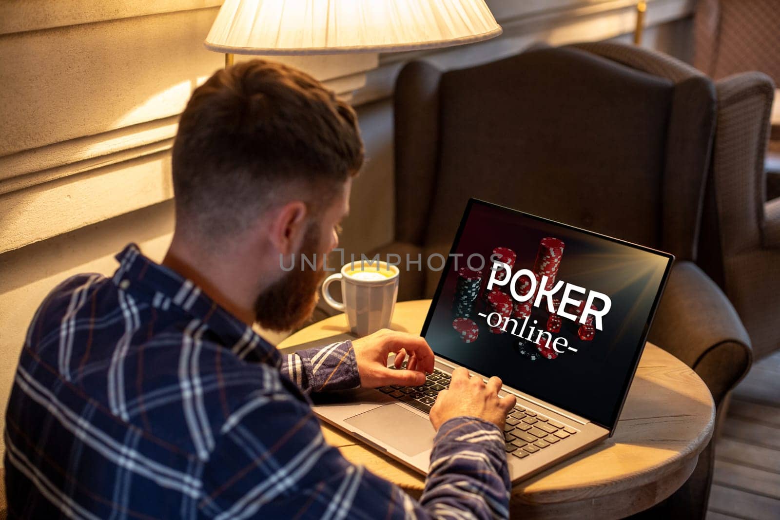 Young man playing poker via netbook during work-break in coffee shop, male sitting in front open laptop computer. by nazarovsergey