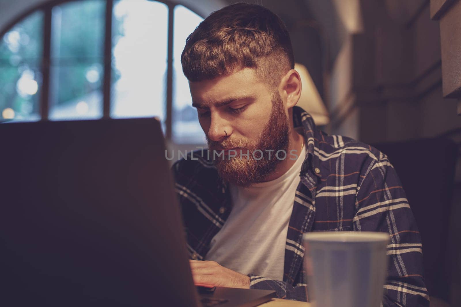 Young professional surfing the Internet on his laptop with cup of coffee on table at coffee shop or home office, working from cafe concept